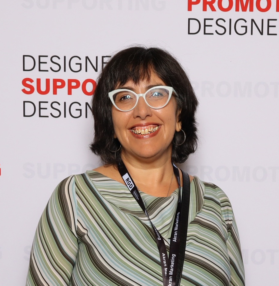 Ruth smiling in front of a backdrop of repeated text while attending the DesignThinkers Conference in Toronto.